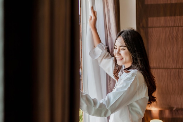 A jovem asiática acorda revigorada pela manhã e relaxa no quarto nas férias. Asiático, ásia, relaxe, sozinho, tecnologia, conceito de estilo de vida.