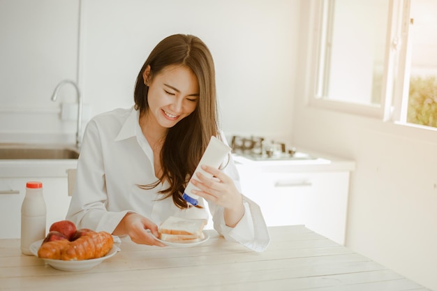 A jovem asiática acorda revigorada pela manhã e relaxante, come café, cereais, pão e maçã no café da manhã em casa de férias. Asiático, ásia, relaxe, café da manhã, atualize, conceito de estilo de vida.