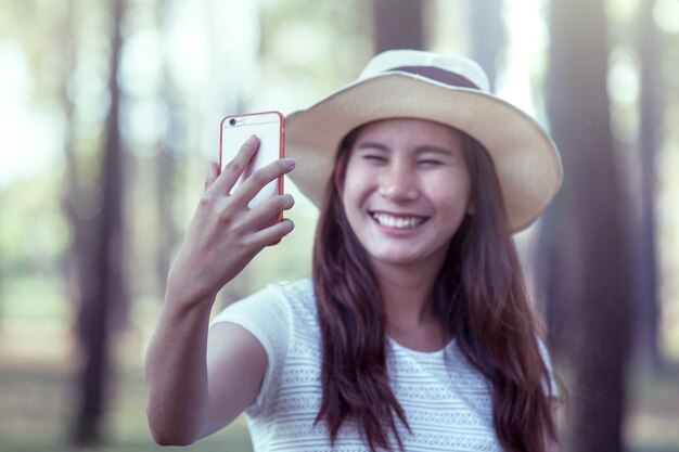 A jovem asiática colocou o chapéu e pegou o selfie no celular no parque em tom de cor vintage