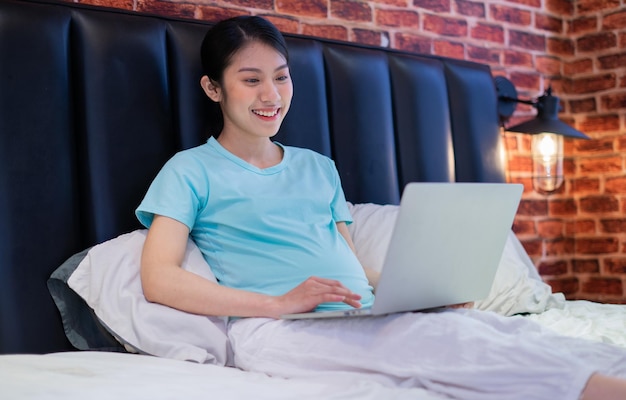 A jovem asiática grávida relaxa em casa