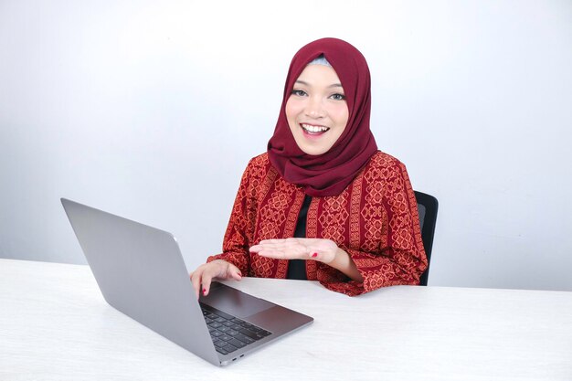 A jovem asiática islâmica está sorrindo apontando a mão ao trabalhar no laptop em fundo branco