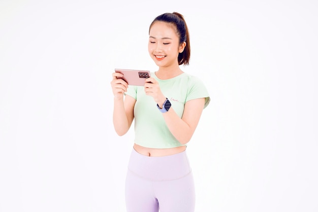 A jovem asiática mostra a tela vazia do smartphone com sorrisos de expressão positiva amplamente vestidos com roupas casuais, sentindo felicidade no fundo azul Celular com tela branca na mão feminina