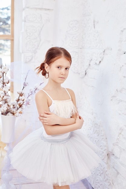 A jovem bailarina está se preparando para uma apresentação de balé. Pequeno balé prima. Menina em um vestido de baile branco e Pointe perto da janela, lindo cabelo ruivo. Jovem atriz de teatro