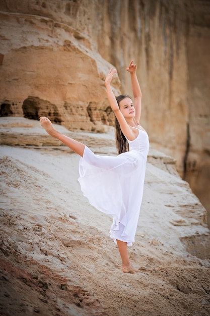 A jovem bailarina faz uma pose elegante à beira de um penhasco arenoso