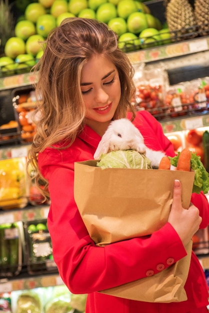 A jovem bonita está comprando legumes para seu coelho branco de estimação no supermercado