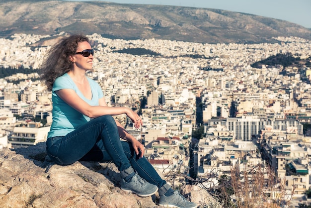 A jovem bonita relaxa com vista para a paisagem urbana de Atenas