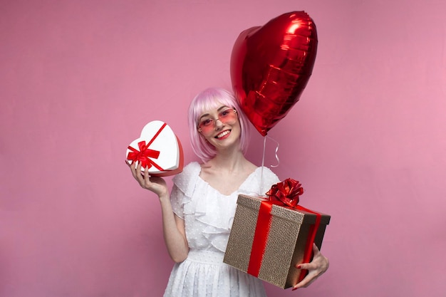 A jovem de cabelo rosa segura balões e presentes e comemora o aniversário de uma mulher com presentes