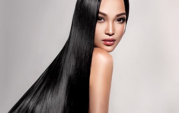 A jovem de cabelos negros com aparência asiática está demonstrando cabelos lisos densos e bem cuidados