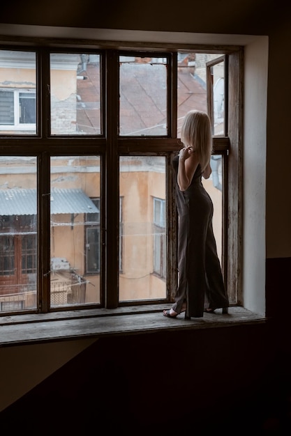 A jovem de terninho preto fica no parapeito da janela grande e olha para o prédio Moldura vertical
