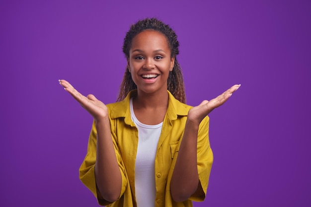 A jovem e alegre mulher afro-americana levanta as mãos com as palmas das mãos levantadas no estúdio