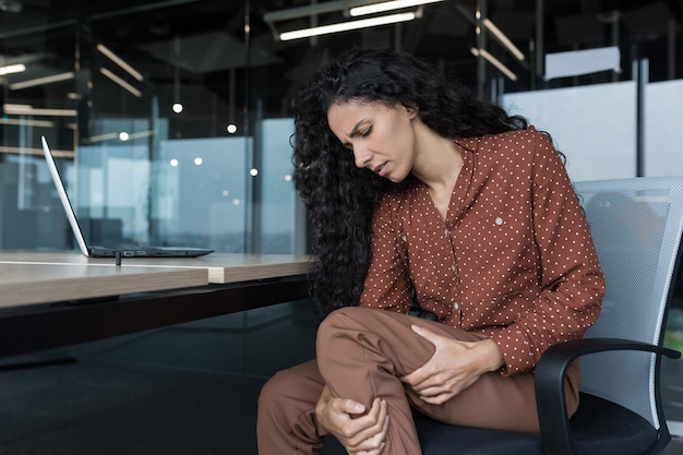 Foto a jovem e bela mulher árabe que trabalha em um escritório moderno com uma mulher de negócios encaracolada de laptop tem dor severa