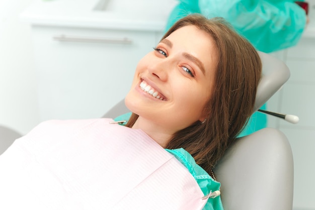 A jovem em êxtase está sorrindo largamente enquanto está sentada na cadeira do dentista Feche a foto com espaço de cópia