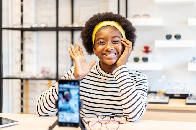 A jovem empresária afro-americana é um vlogger de moda que mostra óculos para celular e sorri vendendo-o on-line ao vivo na loja de óculos