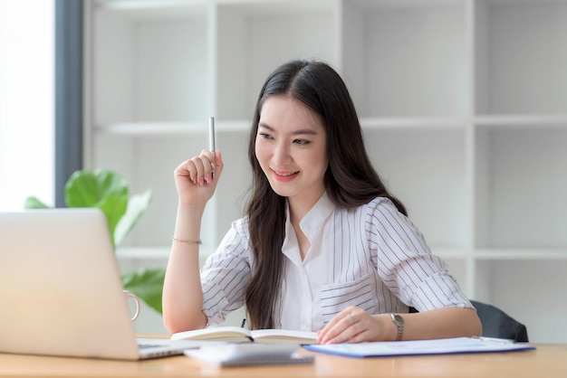 A jovem empresária asiática está feliz em trabalhar no escritório moderno usando um computador portátil.