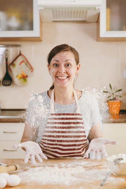 A jovem engraçada alegre sentada à mesa com farinha e vai preparar um bolo na cozinha. Cozinhando em casa. Preparar comida.