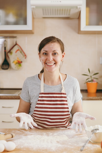 A jovem engraçada alegre sentada à mesa com farinha e vai preparar um bolo na cozinha. Cozinhando em casa. Preparar comida.