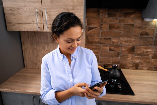 A jovem escreve uma mensagem no smartphone em pé na cozinha.