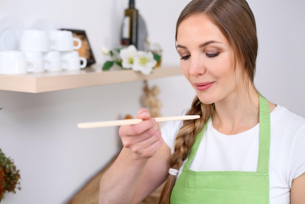 A jovem está cozinhando em uma cozinha a dona de casa está provando a sopa pela colher de pau