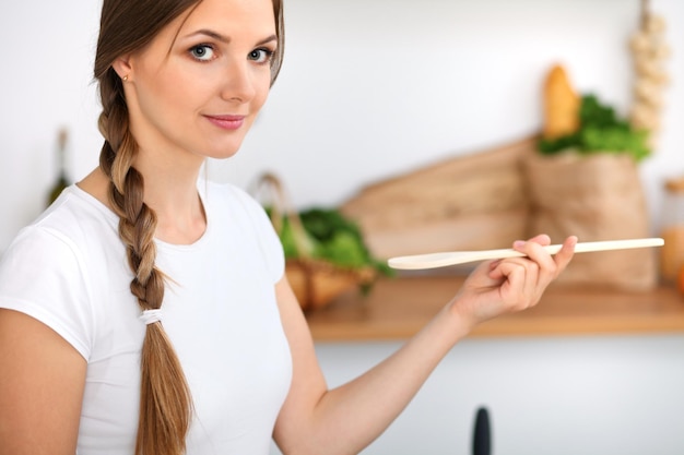 A jovem está cozinhando em uma cozinha A dona de casa está provando a sopa pela colher de pau