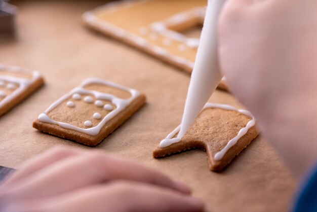 A jovem está decorando o biscoito de biscoitos da Casa de Gingerbread de Natal em casa com cobertura de geada no saco de confeiteiro close-up estilo de vida