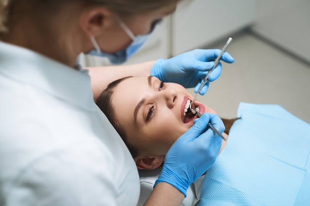 A jovem está deitada na cadeira de dentista enquanto a médica usa instrumentos para o exame