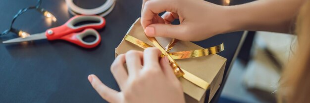 A jovem está embalando presentes embrulhados em papel artesanal com uma fita vermelha e dourada para