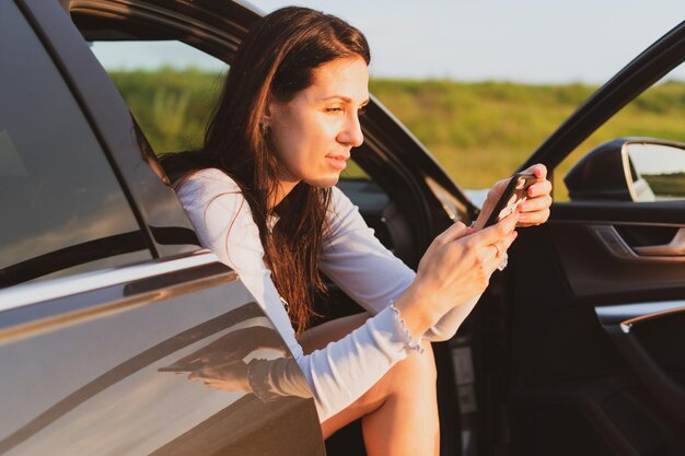 A jovem está viajando nas estradas de carro parado na beira da estrada e tira fotos com um smartphone Conceito de férias