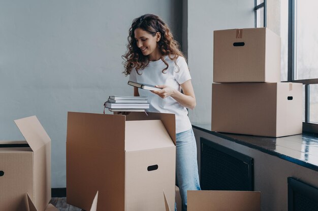 A jovem estudante está alojando-se numa sala residencial mulher europeia a desembalar caixas com livros