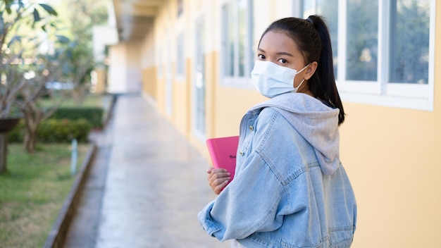 A jovem estudante usa máscara andando na escola.