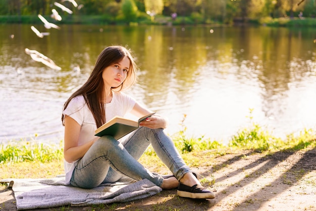 A jovem hipster gosta de sol e um bom dia quente lendo livro enquanto relaxa
