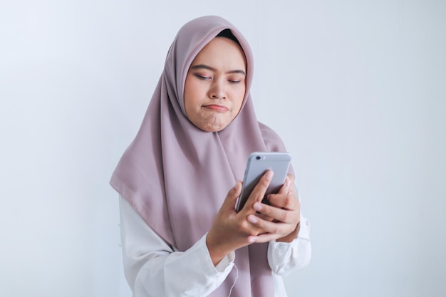 A jovem islâmica asiática usando lenço na cabeça está triste e chora no que vê no smartphone mulher indonésia em fundo cinza