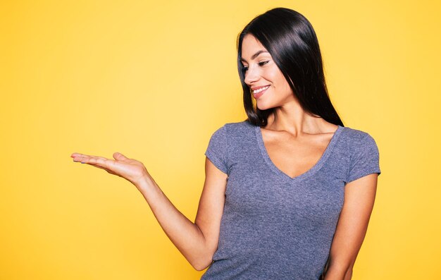 Foto a jovem linda e feliz morena mostra sua palma e sorrindo isolada em fundo amarelo