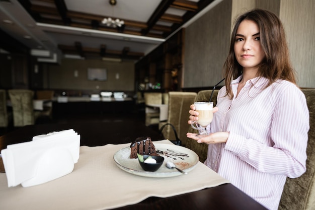 A jovem linda morena senta-se no café restaurante dentro de casa e bebe café com leite
