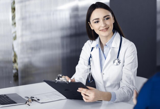 A jovem médica sorridente está preenchendo as recomendações médicas usando uma prancheta. Terapeuta no trabalho em um escritório de clínica. Conceito de medicina.