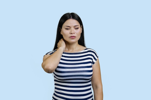 A jovem morena asiática está sofrendo de dor no pescoço isolada em azul pastel