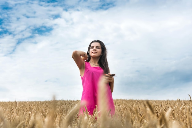 A jovem mulher bonita em um vestido anda em um verão dourado do campo de trigo