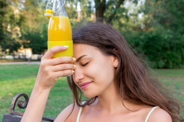 A jovem mulher bonita tenta se refrescar com uma bebida fria de suco em um dia quente de verão