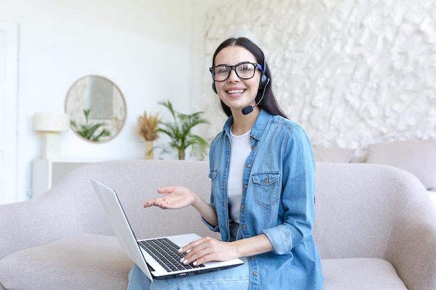 A jovem mulher bonita trabalha como operadora on-line em casa, ele se senta em casa no sofá com um