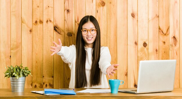 A jovem mulher chinesa que estuda na mesa dela se sente confiante dando um abraço para a câmera.