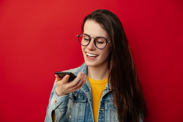 A jovem mulher de sorriso nos monóculos que guarda o telefone fala ativa o assistente de reconhecimento de voz digital virtual no smartphone, mensagem feliz do registro da assistência da Internet do comando da menina, conceito da tecnologia