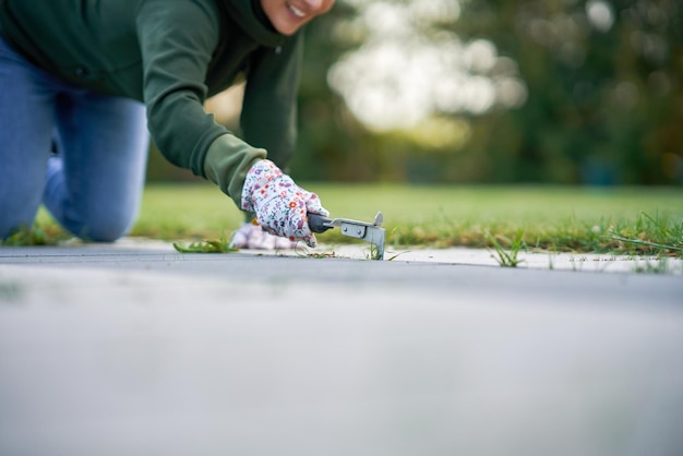 A jovem mulher extrai as ervas daninhas do concreto no jardim