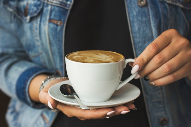 A jovem mulher segurando a xícara de café nas mãos dela