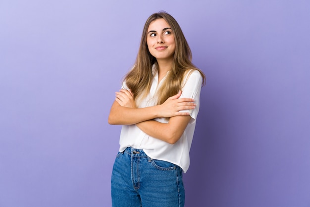 A jovem mulher sobre o fundo roxo isolado que faz dúvidas gesticula ao levantar os ombros