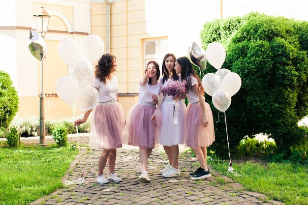 A jovem noiva está de pé com um lindo buquê, e amigas se divertem atrás dela