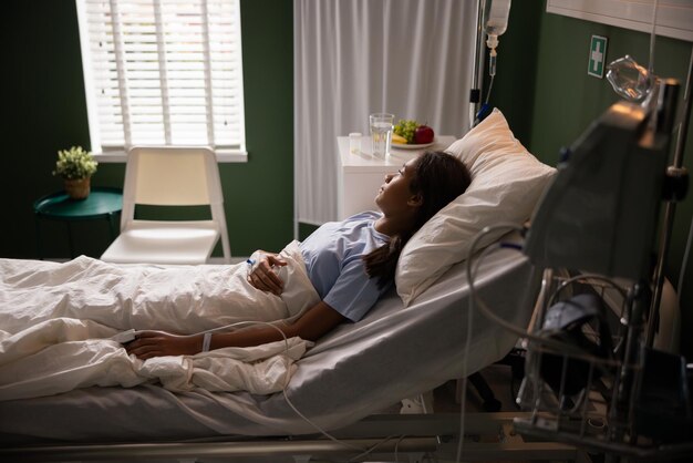 A jovem paciente está deitada em sua cama de hospital olhando felizmente pela janela.