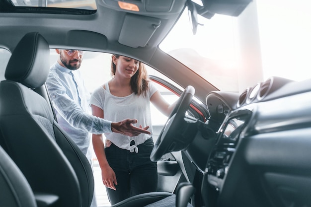 A jovem positiva faz uma visita ao salão de automóveis e escolhe o gerente de carros ajudando-a