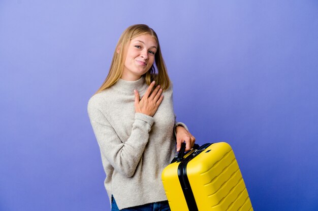 A jovem russa segurando a mala para viajar tem uma expressão amigável, pressionando a palma da mão no peito. Conceito de amor.