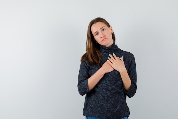 A jovem triste está apertando as mãos no coração no fundo branco