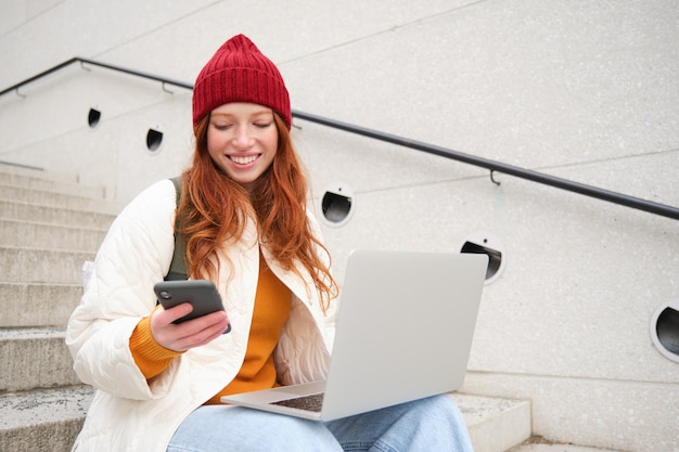 A jovem turista que reserva um quarto de hotel no laptop insere o código de confirmação no smartphone sentado com