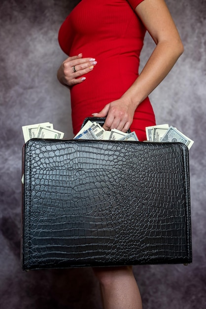 A jovem usa um vestido vermelho segurando notas de dinheiro cheias de dólares em uma maleta preta
